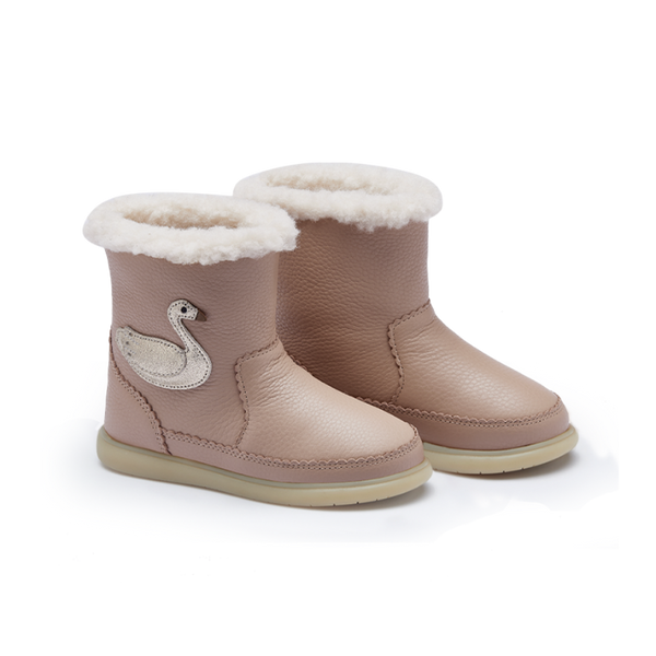 A pair of toddler ankle boots in a dusty pink color, featuring a white wool lining at the top, a white swan applique on the side, and a light beige sole.