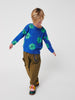 Child wearing a blue sweater with green patterns and brown pants on a white background