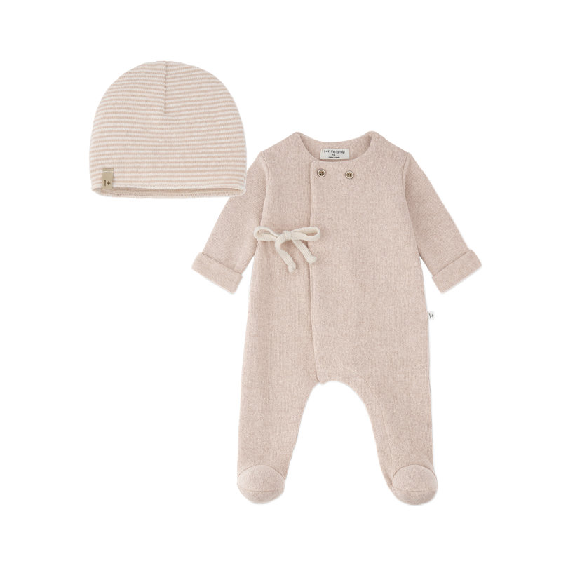 A baby footed one-piece sleeper in a soft oatmeal beige color with a matching striped knit beanie hat