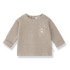 A light beige knit long-sleeve top for toddlers, featuring a small chest pocket with a decorative button and a visible 'living baby' brand label inside the collar