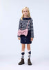 Young girl wearing a striped sweater, skirt, and patterned socks with a pink bag